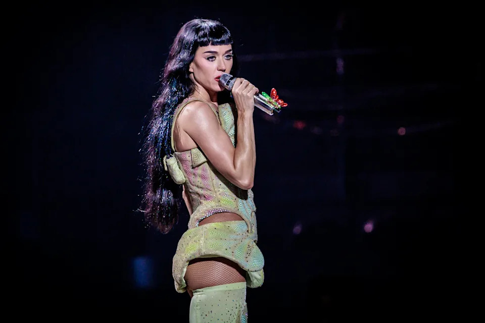 Performer in a futuristic, form-fitting outfit singing on stage with a microphone