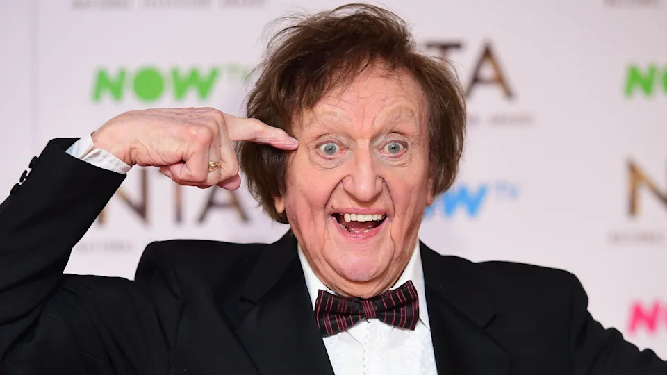 Dodd at an awards ceremony in 2017. He smiles, opened-mouth with his finger points to his temple.