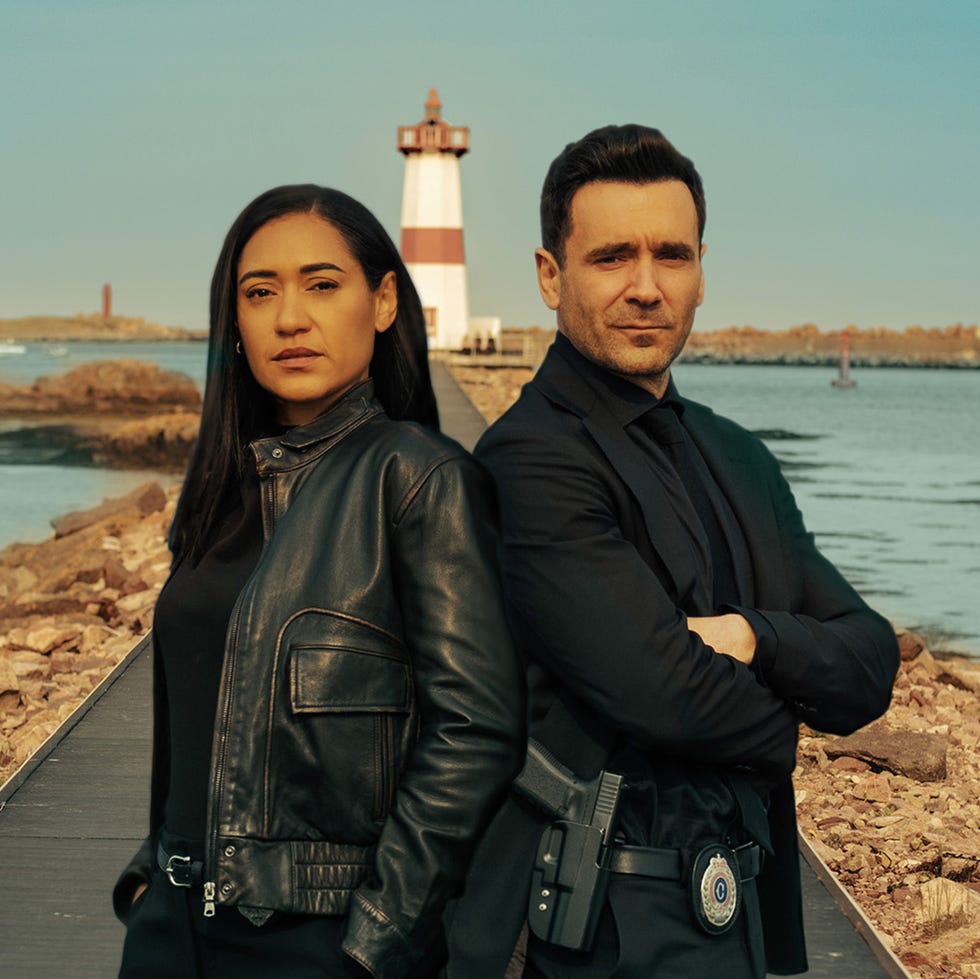 two people standing on a walkway by the water with a lighthouse in the background