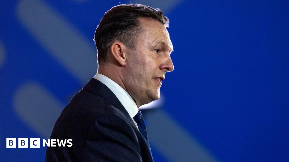 Russell Findlay, who has short black hair, in profile against a blue background. He is wearing a business suit