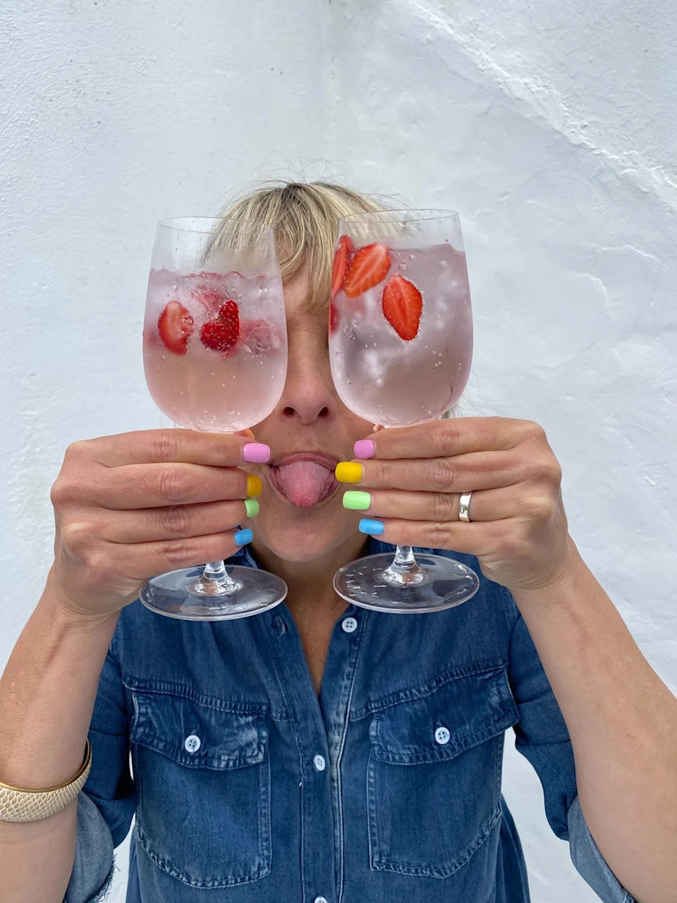 Person holding two glasses of sparkling water with strawberries, playfully sticking out their tongue