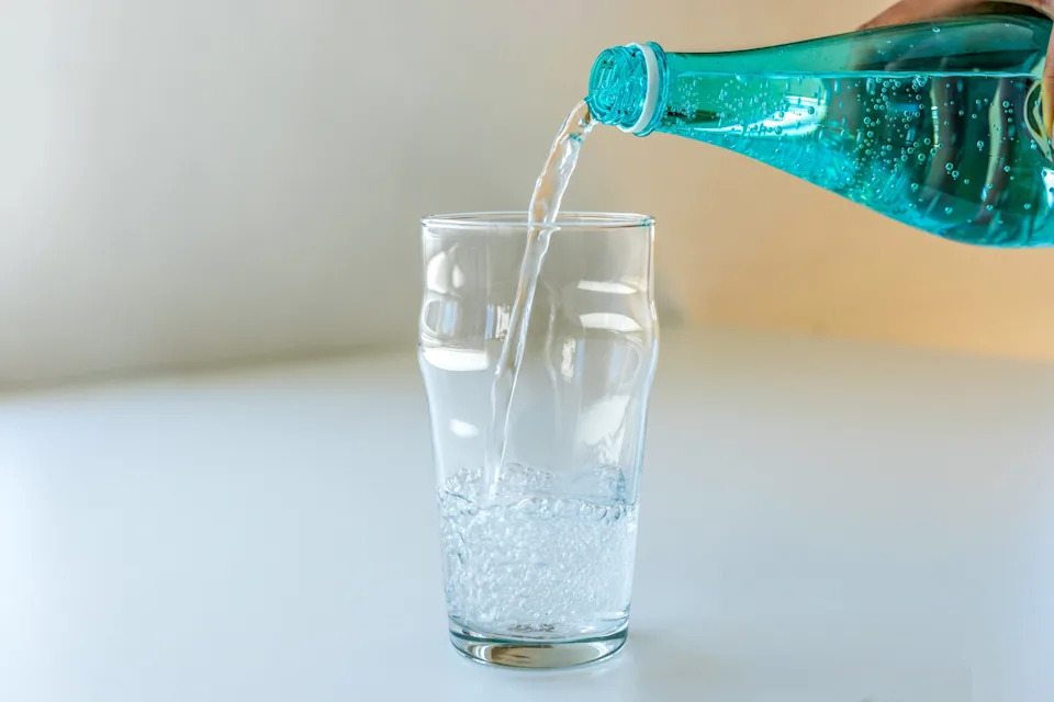 Sparkling water is poured from a bottle into a clear glass on a white table