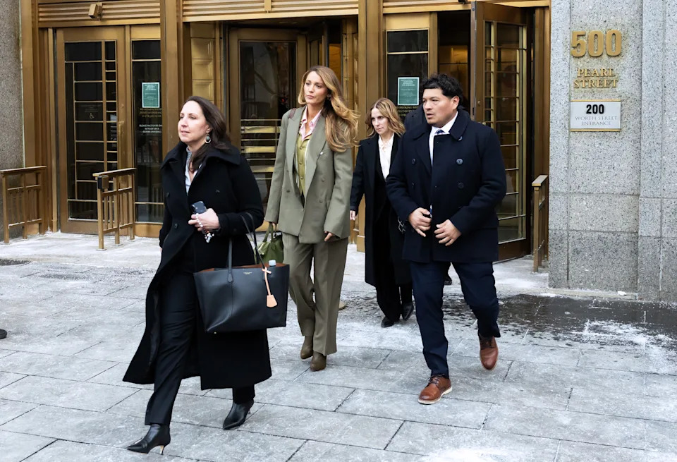 Group of individuals exiting a building, including a person in a tailored suit with no tie, accompanied by others in professional attire