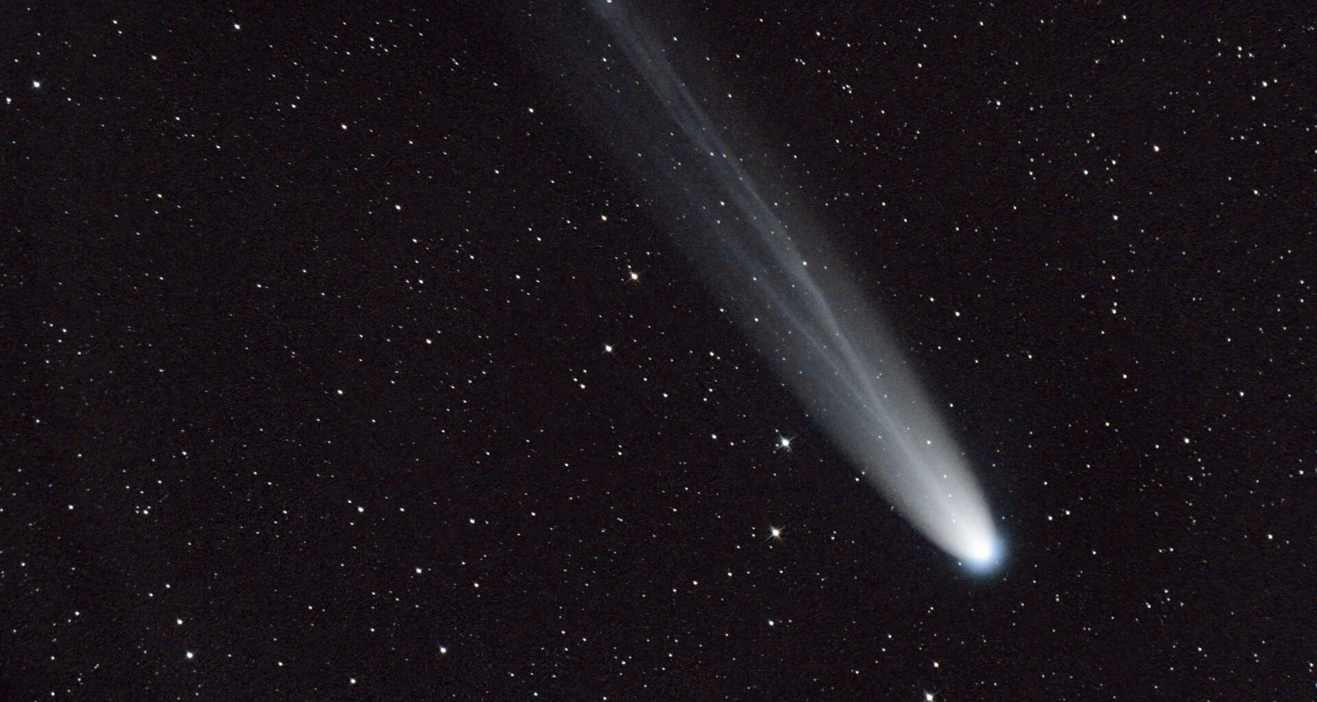 A streak of white across a dark starry night sky shows a comet moving toward the bottom right of the image.