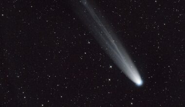 A streak of white across a dark starry night sky shows a comet moving toward the bottom right of the image.