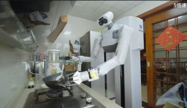 A white humanoid robot stands over a kitchen stove, holding utensils.