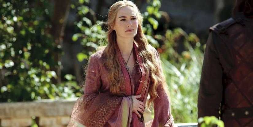 Cersei Lannister wearing a red and yellow dress in a garden talking to someone in Game of Thrones season 1