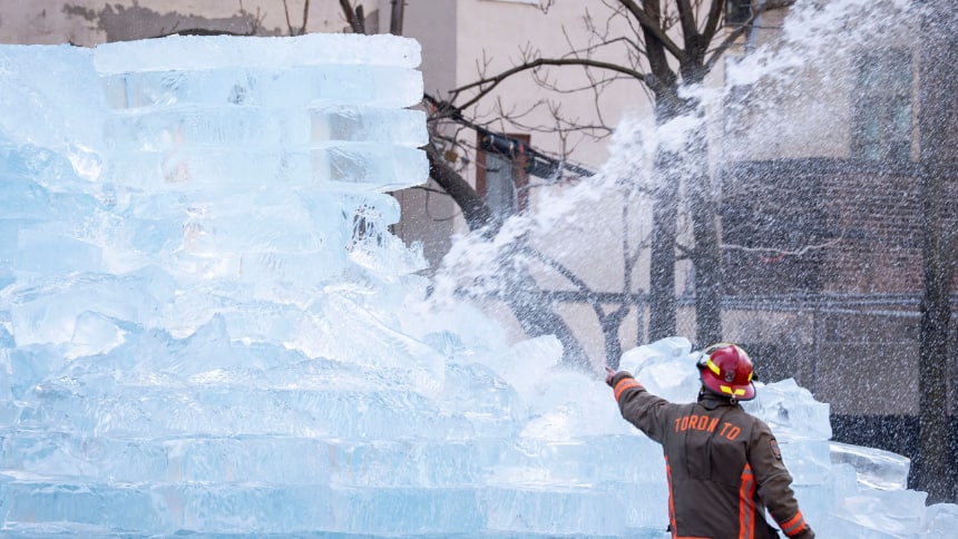 A fireman stands in front of the large ice structure with water being sprayed at it.