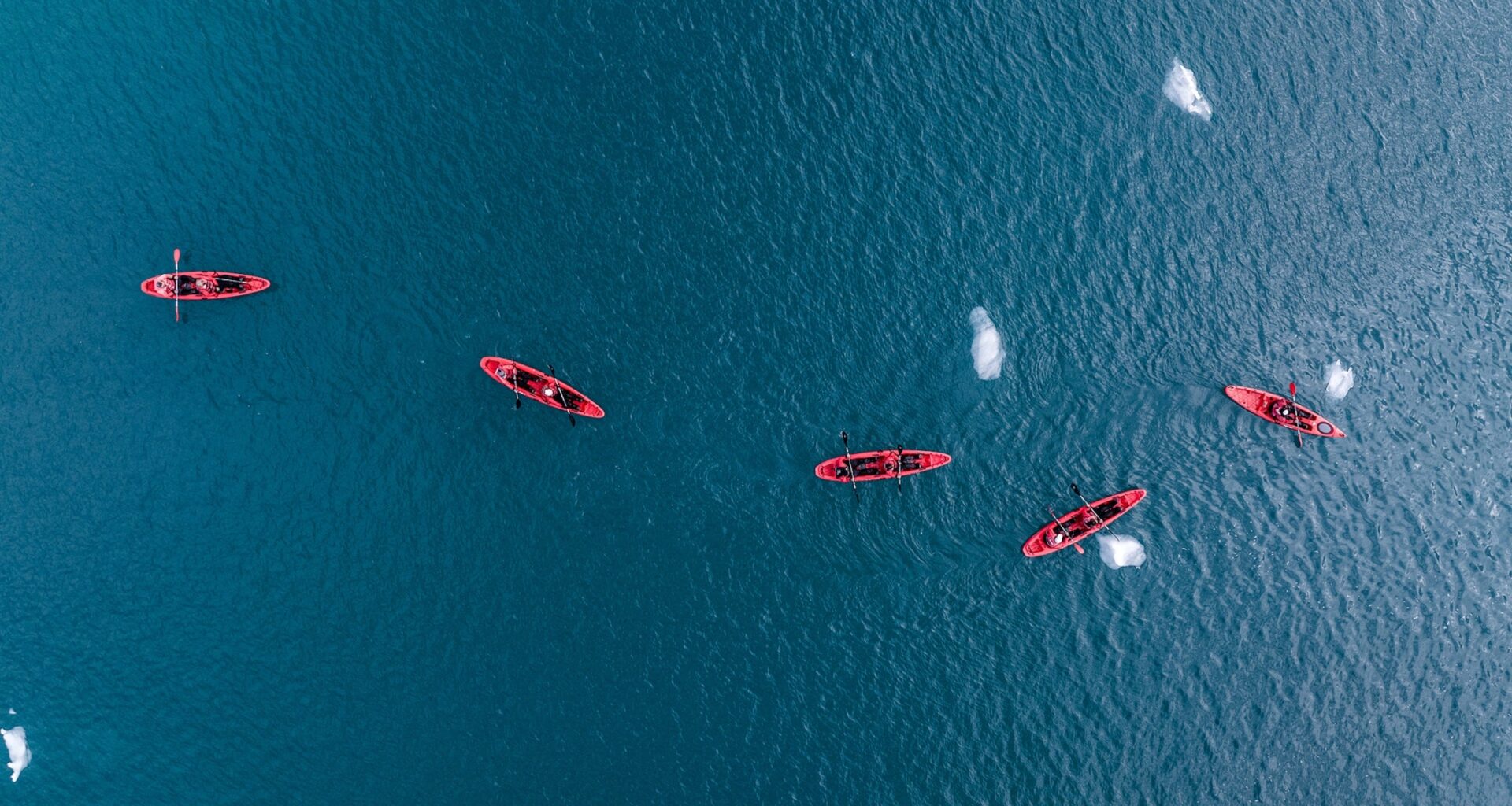 A sea kayak floating in the icy blue waters of Svalbard, Norway, near a rocky coastline