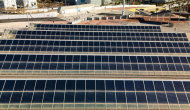 Rows of large solar panels sit on the ground in an industrial area.