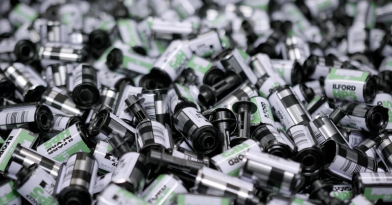 A large pile of black and silver 35mm film canisters with green and white labels, predominantly showing the ILFORD brand.