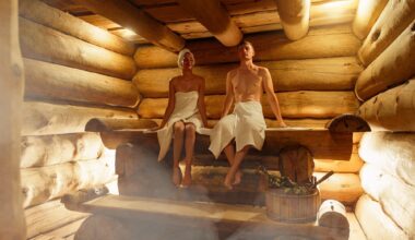 Young couple relaxing and sweating in hot sauna wrapped in towel. Woman and man In Sauna. Interior of Finnish sauna, classic wooden steam room with hot steam. Russian bathroom. Relax in hot Bathhouse.