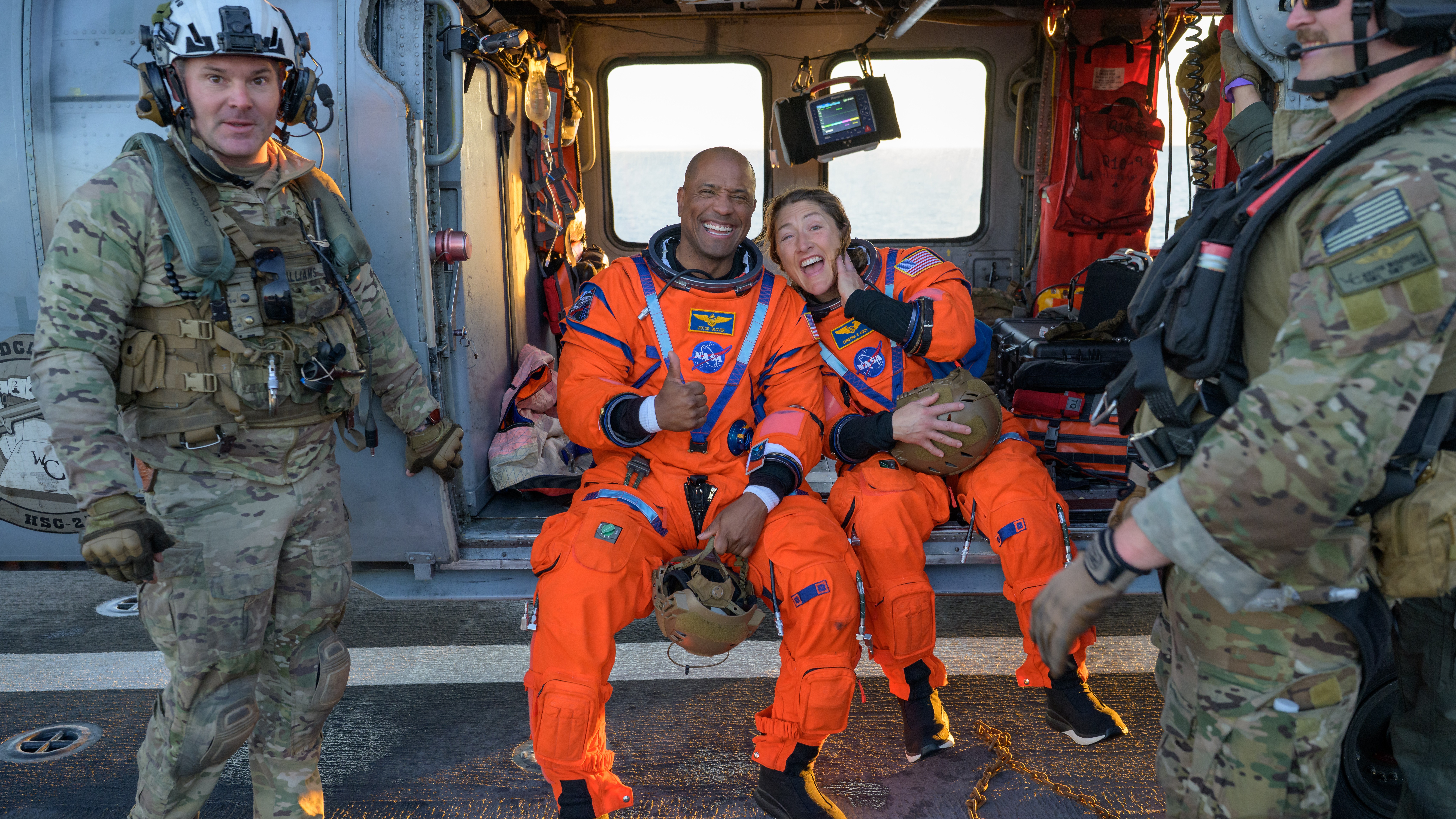 NASA astronaut Victor Glover, Artemis II pilot, left, and NASA astronaut Christina Koch, Artemis II mission specialist are seen sitting on a Navy MH-60 Seahawk.