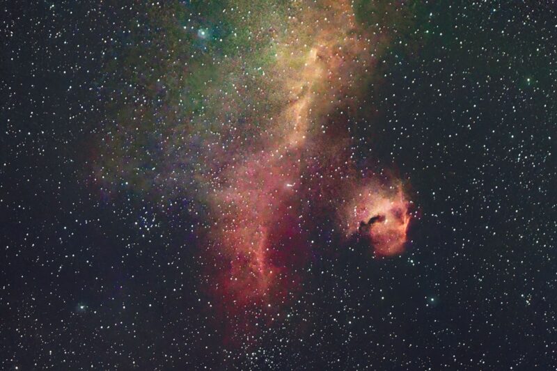 A long, wispy, glowing red and green space cloud and a smaller round one, among numerous stars.