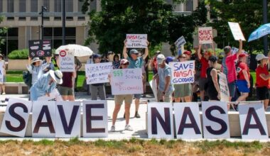 People hold signs outside on a sunny day in protest of NASA budget cuts, July 20, 2025.