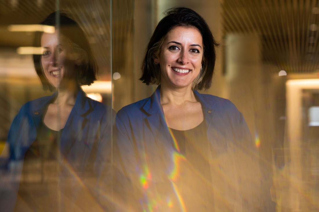 A portrait of Leila Deravi against a glass wall in a hallway