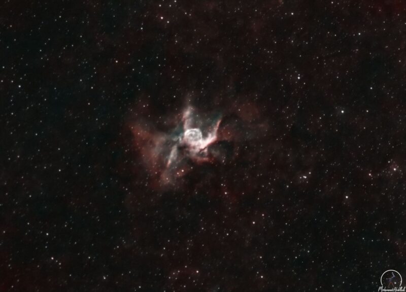 A large, pink cloud of gas in a wispy H shape, plus numerous faint stars.