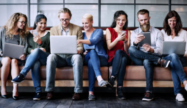 people sitting on a sofa and looking at phones and laptops.