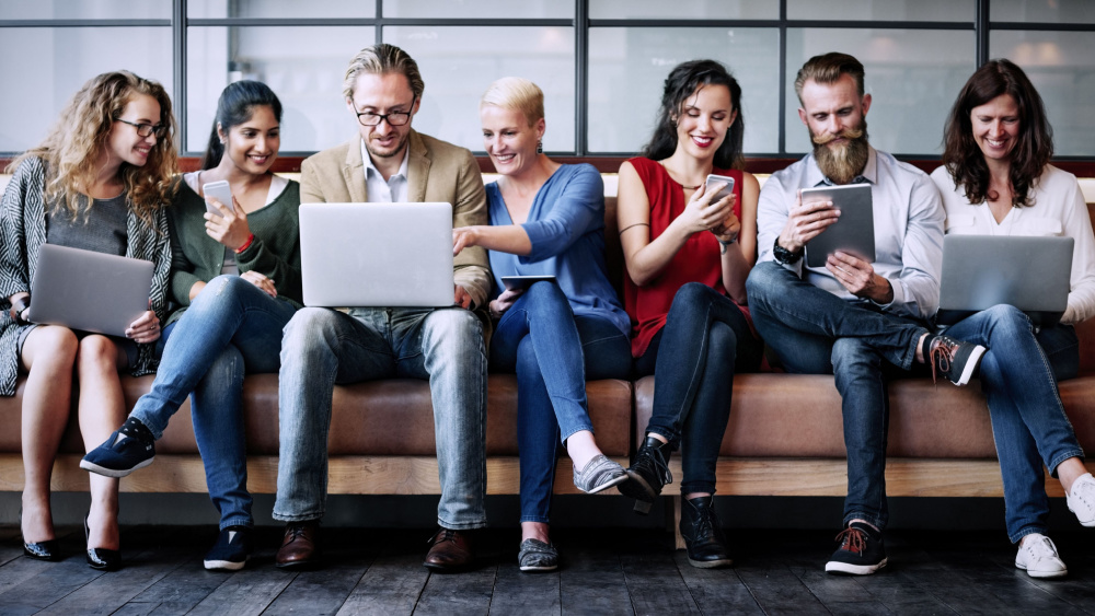 people sitting on a sofa and looking at phones and laptops.