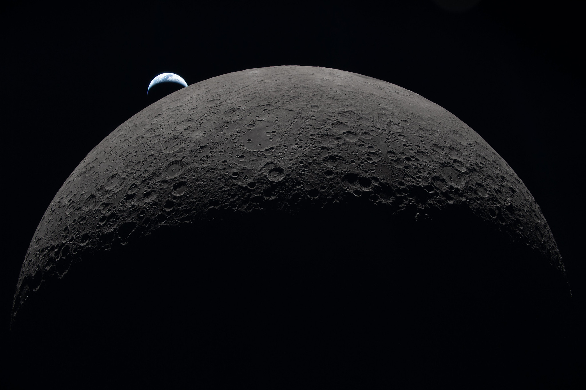 A tiny Earth is in the background above the horizon of the moon.