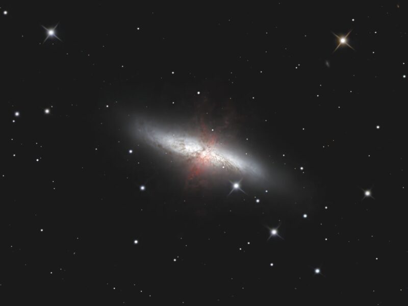 Oblique view of a galaxy with pink wisps toward the middle and sparse foreground stars.