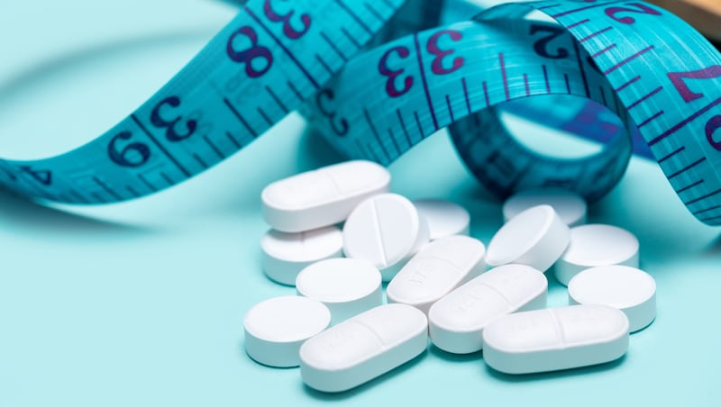 Pills spilling out of pill bottle and measuring tape on blue background