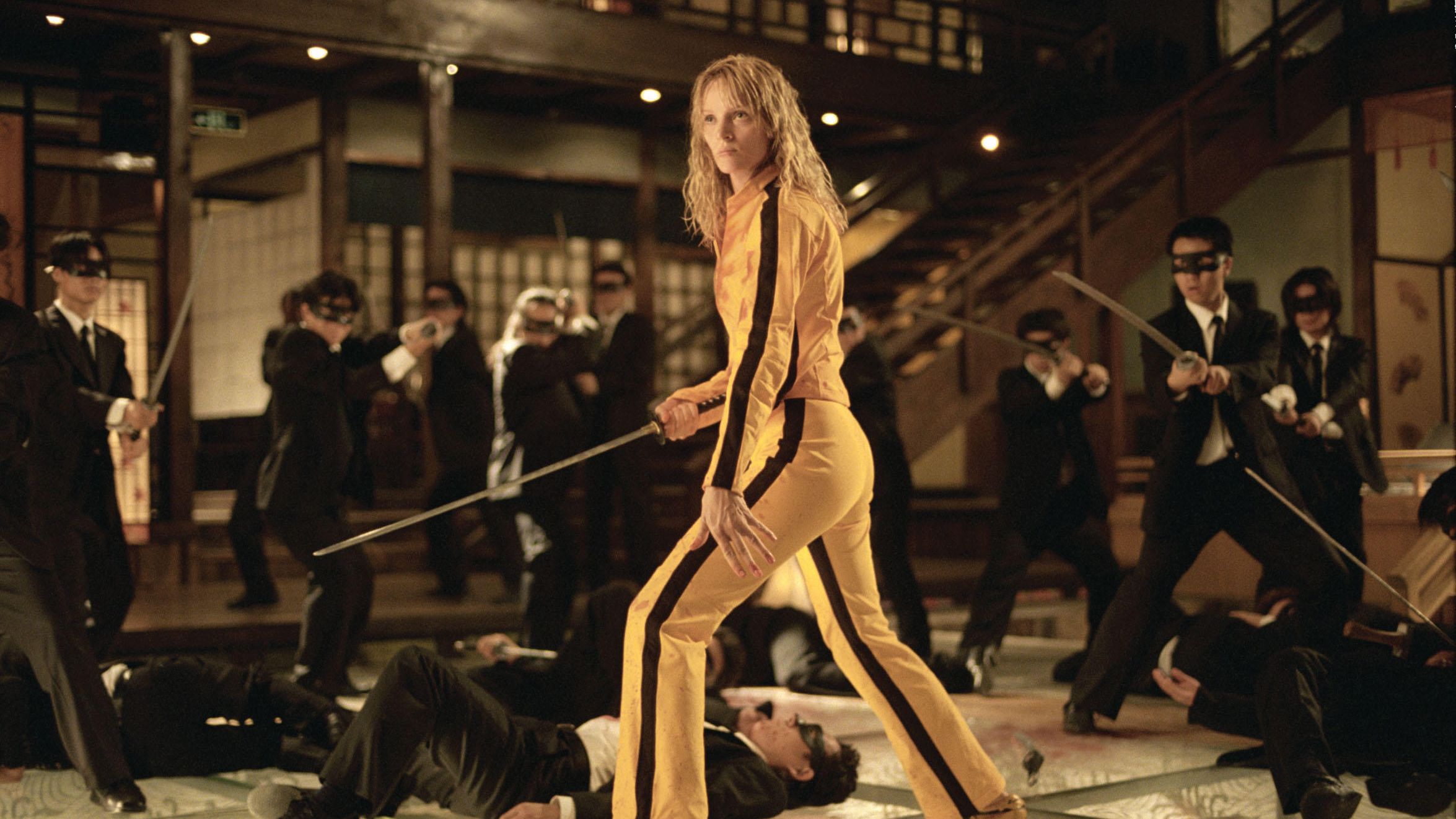Uma Thurman as The Bride, in a yellow jumpsuit and holding a sword, is surrounded by the Crazy 88 Yakuzas in Kill Bill Vol. 1