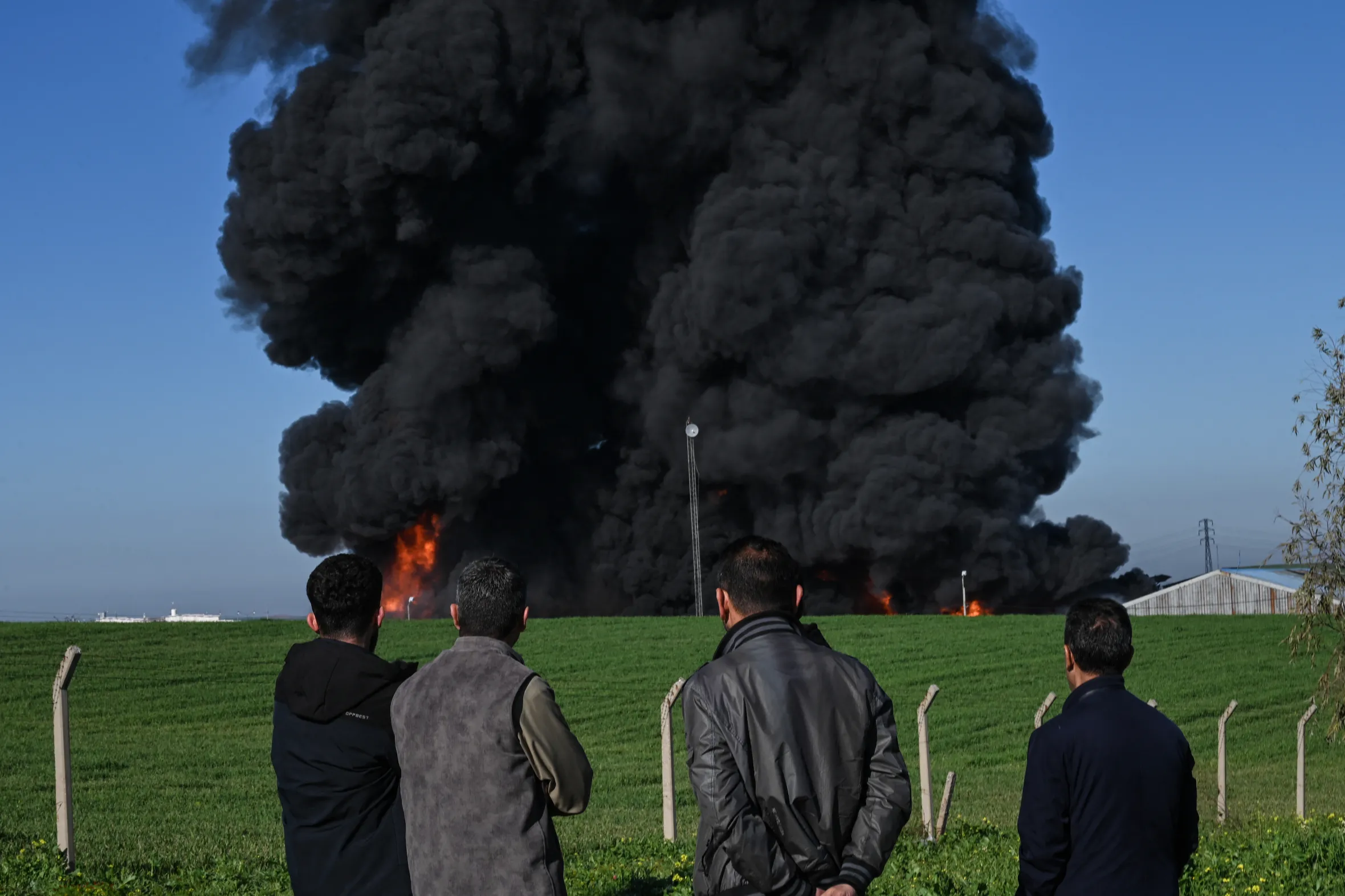 People watch as smoke billows from an oil warehouse following a suspected drone strike in Erbil, Iraq.