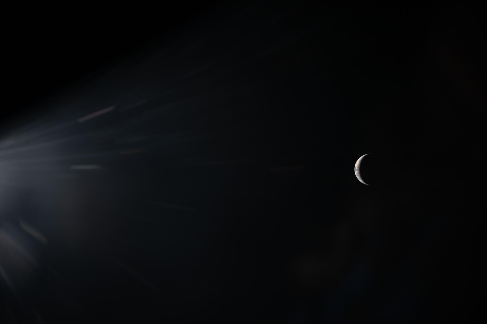 A crescent moon appears on the right side of a dark sky, with light rays streaming in from the left—echoing the hope and wonder inspired by Artemis II as it journeys between Earth and the Moon.