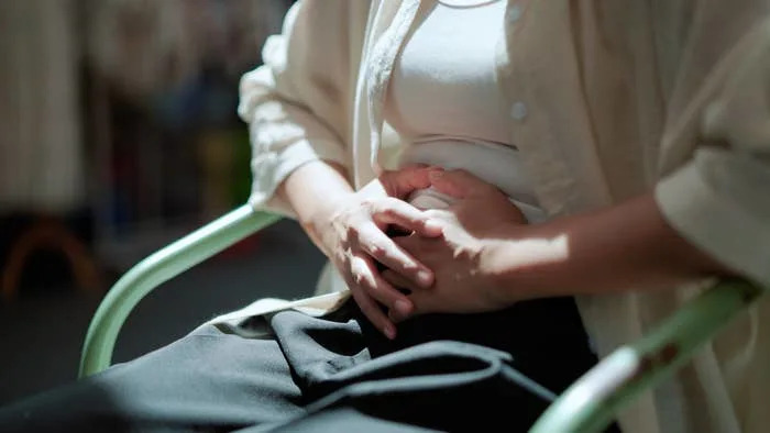 A person sits on a chair, resting hands on their stomach, suggesting a focus on digestion or culinary experience
