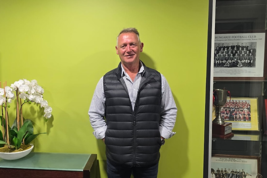 A man in a puffer jacket stands in front of a yellow wall