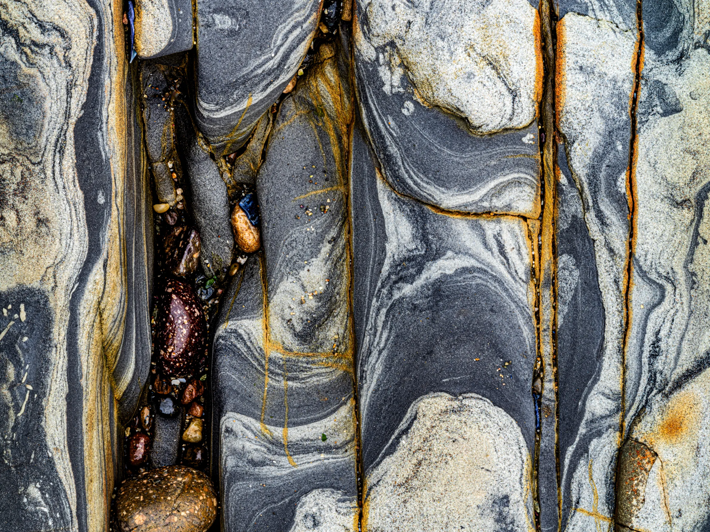 Patterns of grey, white, black, and orange rock shaped over millennia along the Northern California coastline.