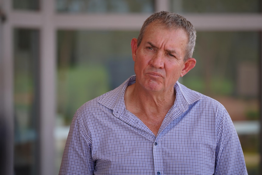 A man wearing a collared shirt pulls a straight lipped thinking face with squinting eyes.