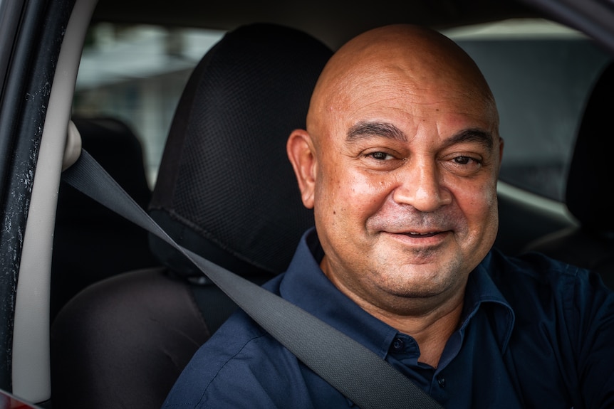 A man smiles while sitting in his car.