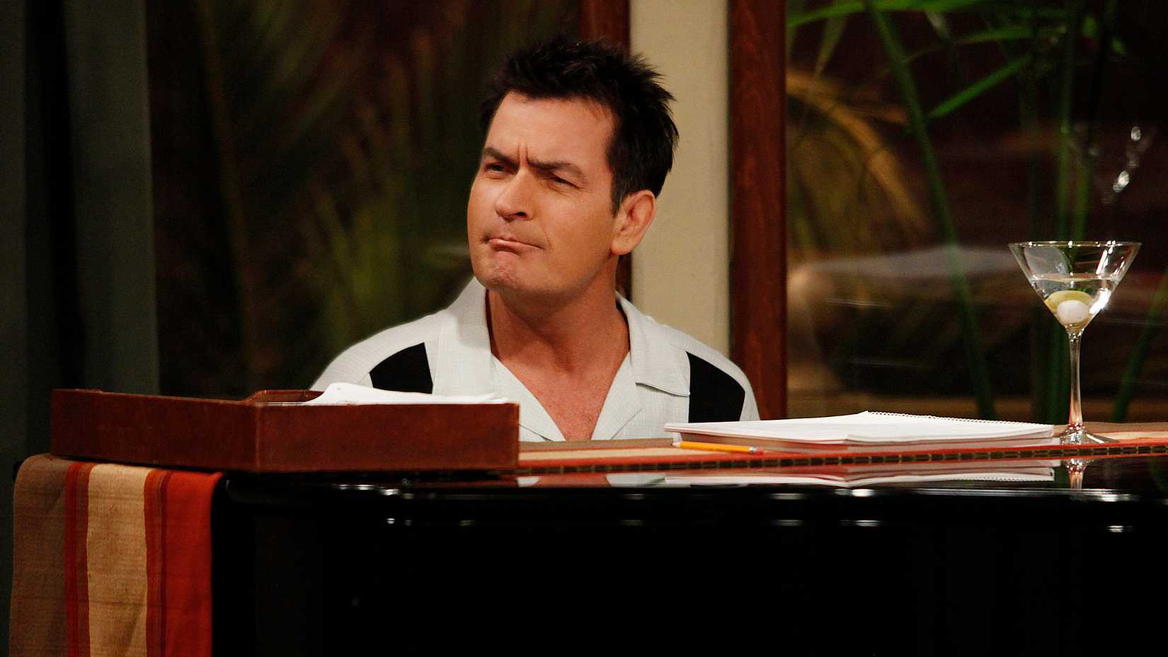 Charlie Sheen sitting behind a piano on Two And A Half Men, pursing his lips.