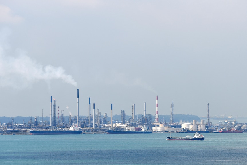 Chimneys and storage tankers next to a bay with a tanker on the water.