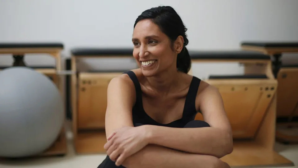  Woman smiling sitting down doing bodyweight Pilates workout. 