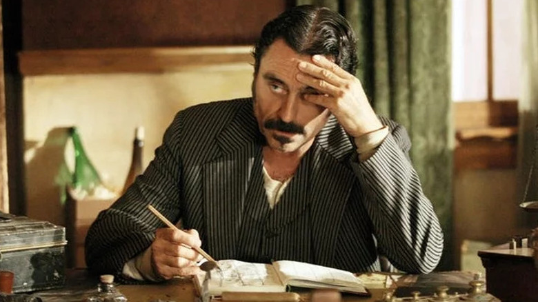 Al Swearengen (Ian McShane) puts his head in his hand as he writes in a ledger in Deadwood