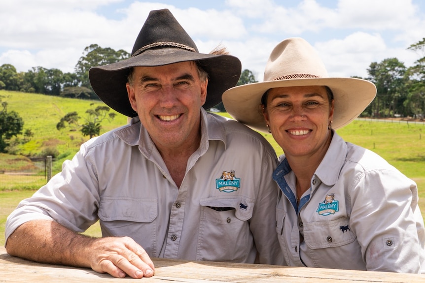 A smiling couple with rolling green hills behind them.