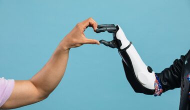 A person's left hand comes from left of the image to meet a black and white robotic hand from the right of the image to make a heart with their hands in the center, all in front of a blue background.