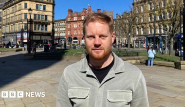 A man with a ginger beard and strawberry blond hair wearing a light grey/green shirt and black T-shirt standing in Bradford city centre
