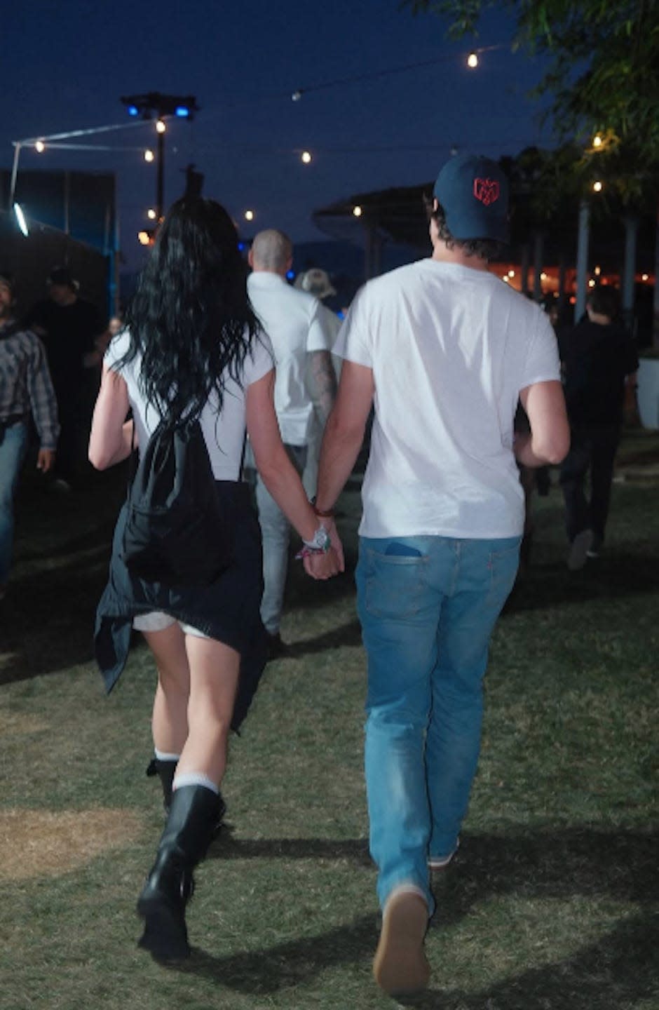 Couple walking hand in hand at an outdoor event during the evening.