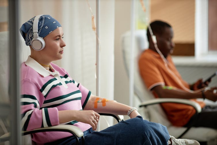 Two patients in chairs with IVs attached to their arms, wearing street clothes, headphones over their ears
