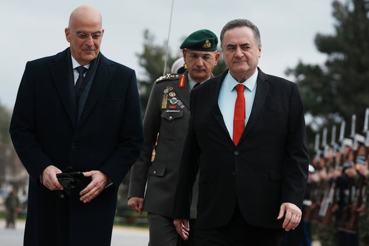 Two men in overcoats walk past a row of soldiers.