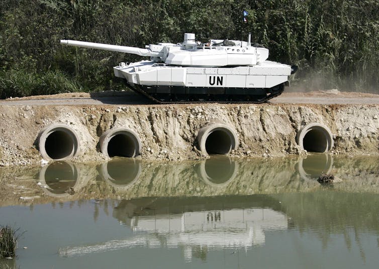 A tank drives on a bridge next to a river.