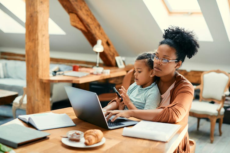 A woman working on a laptop while also supervising a child