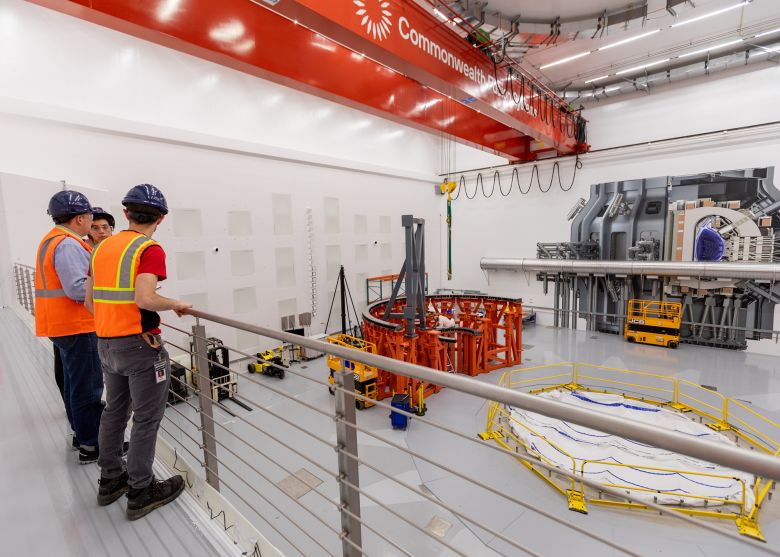 Workers assemble a frame that will hold Commonwealth Fusion's SPARC tokamak demonstration system, center, and a life-size rendering of the device on the far wall, at the company's campus in Devens, Massachusetts, in November 2024.