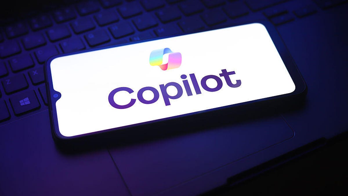 A phone on a laptop shows the Copilot logo on a white screen.