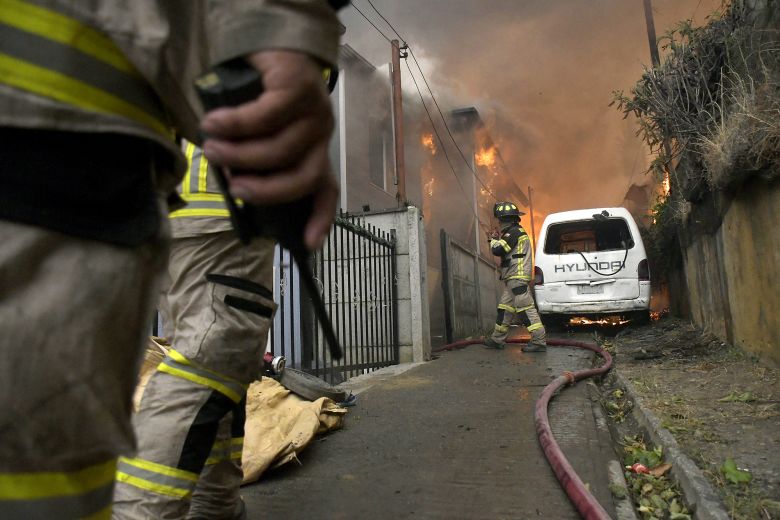 Firefighters try to extinguish a burning house during a wildfire in Concepción, Chile, on January 18, 2026.