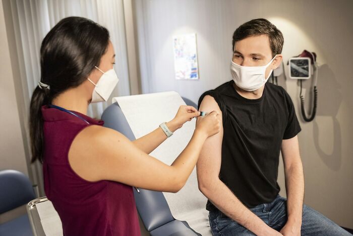 Healthcare worker in mask administering vaccine to young man in clinic, highlighting donorcycle healthcare safety measures.